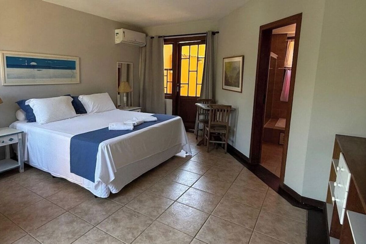 A hotel room with a bed, a desk, a chair, and a bathroom door.