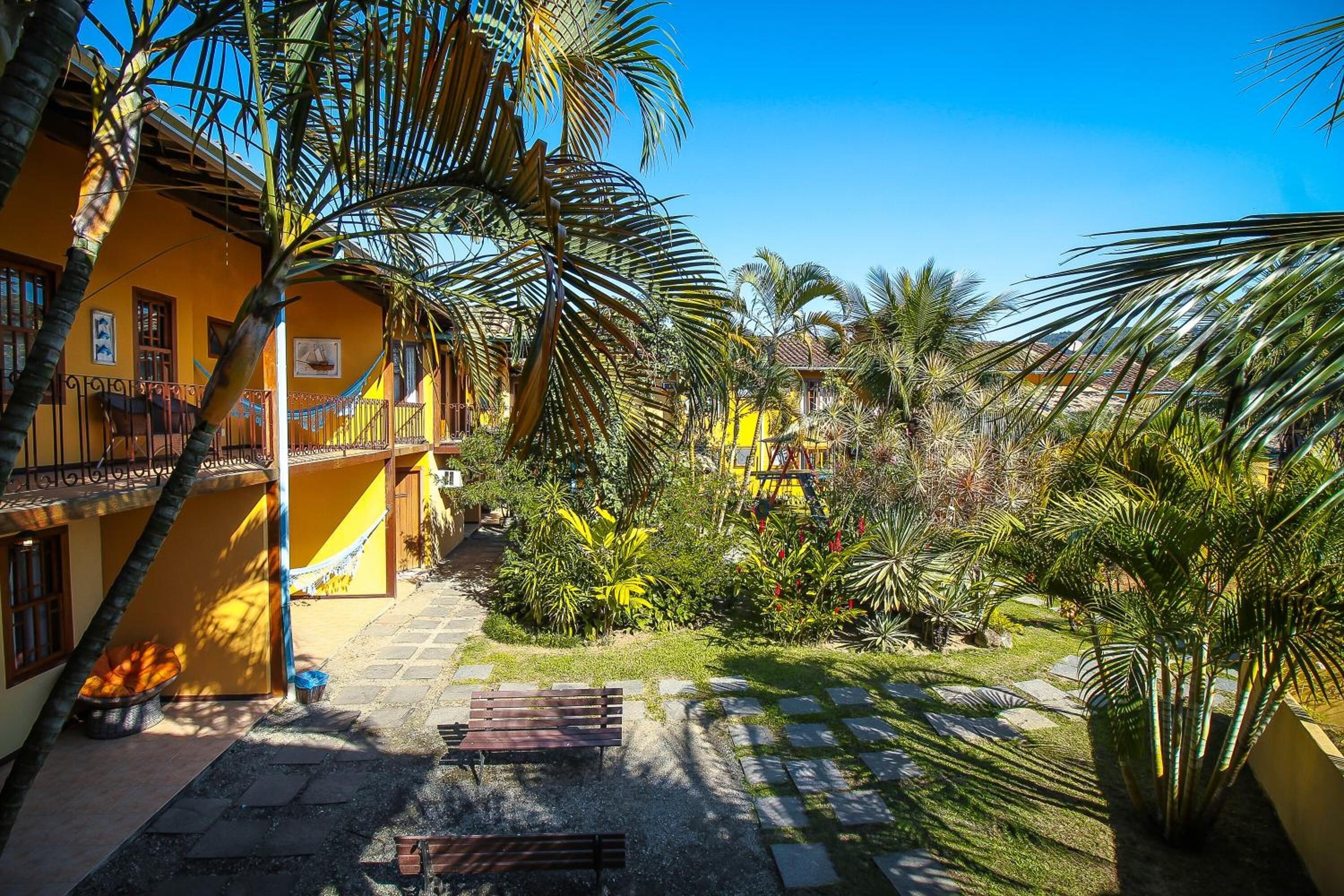 Un patio con un edificio amarillo, palmeras y una hamaca.