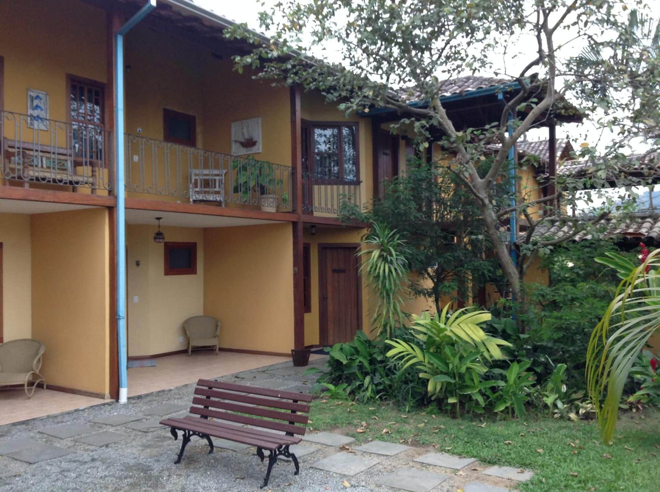A two-story building with a balcony, a bench, and various plants.