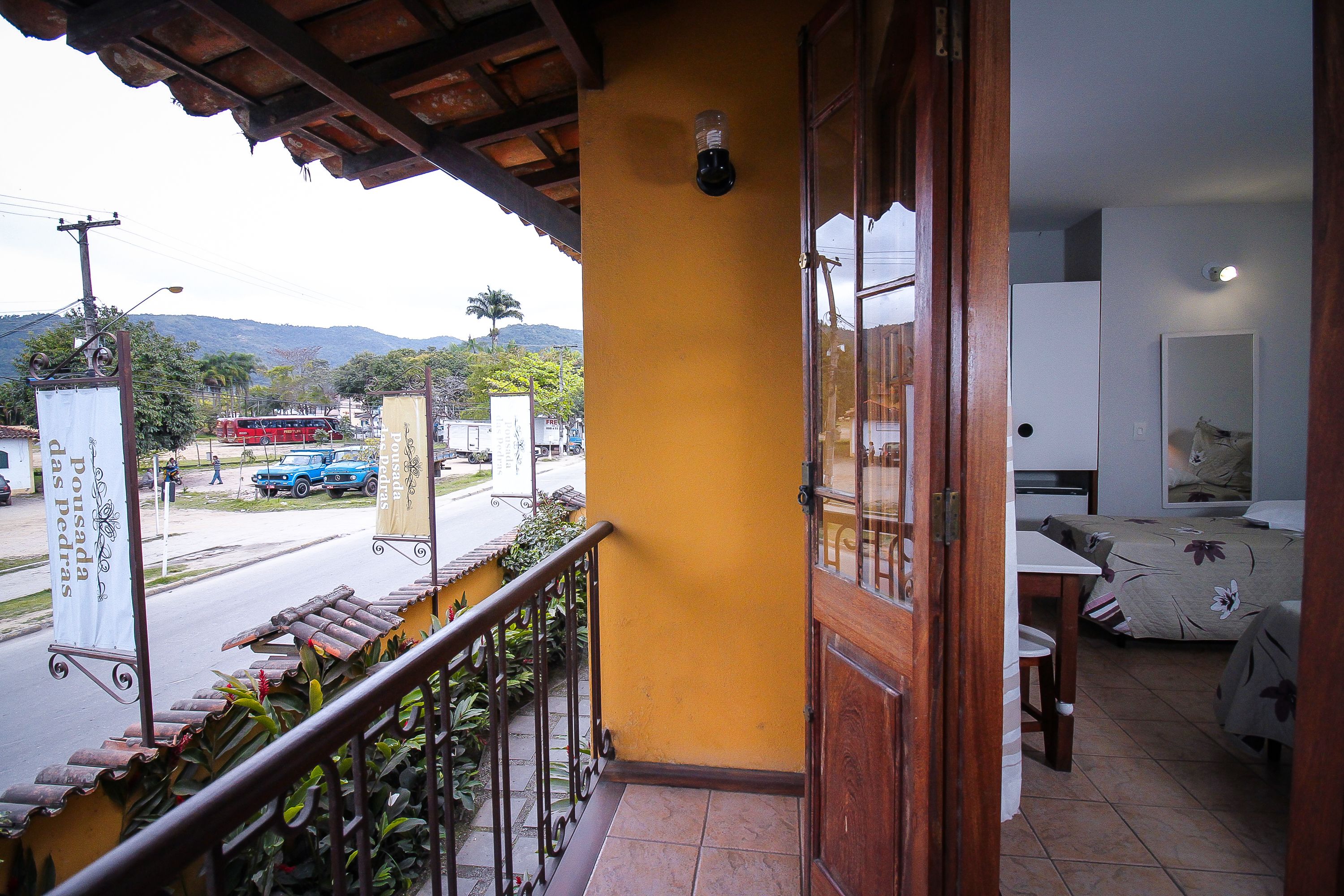 A balcony with a view of a street and mountains. There is a wooden railing and a tiled floor.