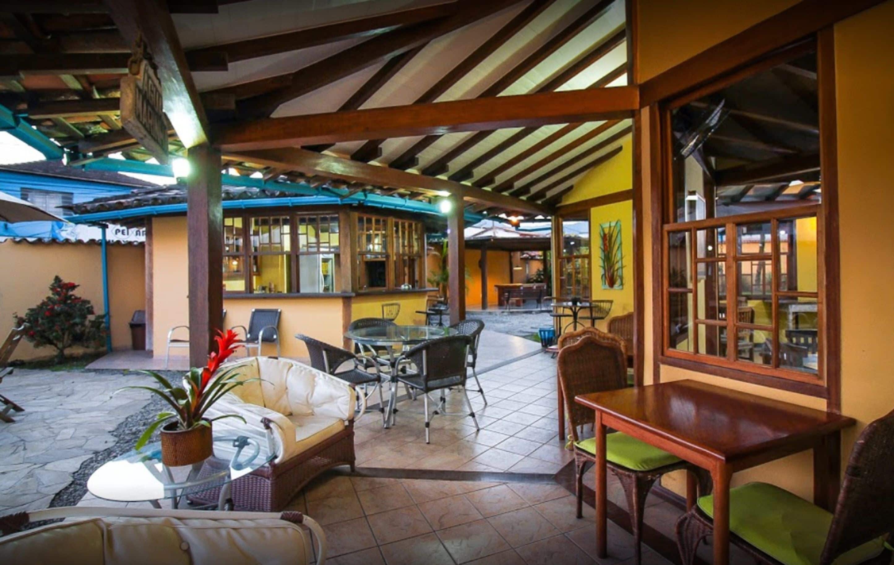 Un patio al aire libre con una pérgola de madera, mesas de vidrio, mobiliario de mimbre y vistas al área del bar interior.