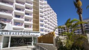A multi-story hotel with balconies, a prominent vertical wooden panel, and a palm tree in the foreground. - Hotel Ambassador Playa II (Benidorm)