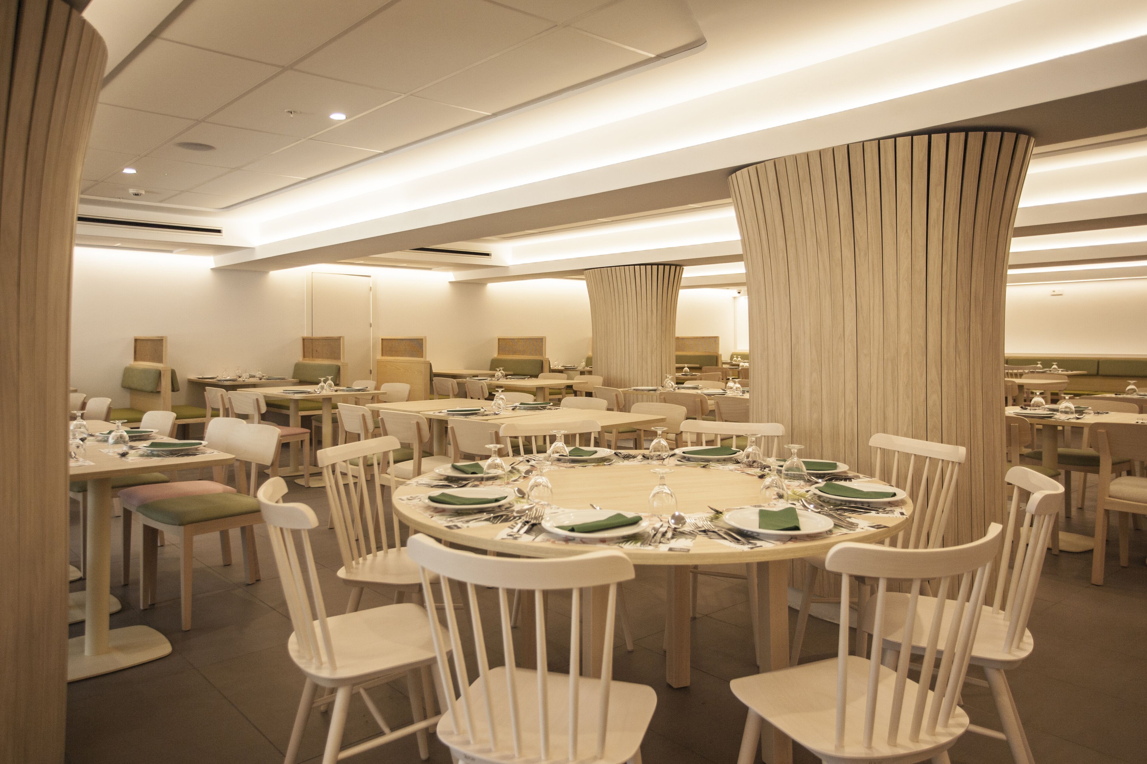A spacious dining area with multiple round tables, each set with white chairs and green tablecloths.