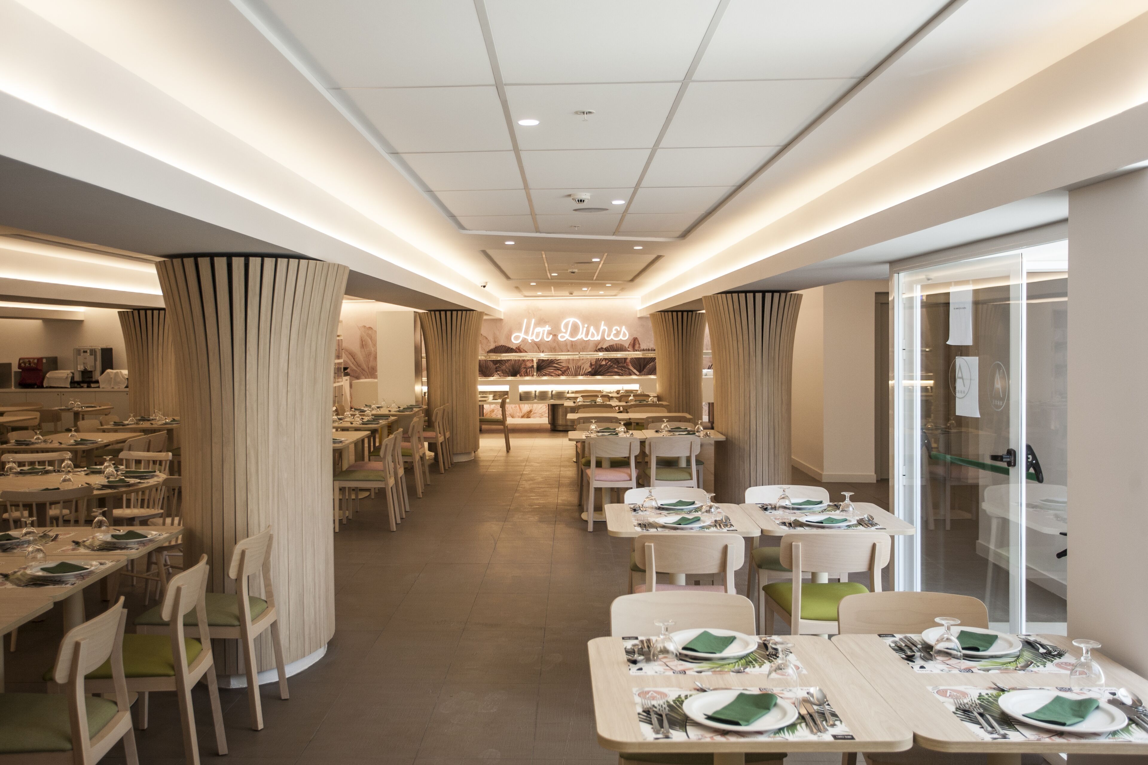 Un restaurante moderno con mesas y sillas ordenadas, un letrero central que dice 'Hot Dishes' y una decoración interior limpia y contemporánea.