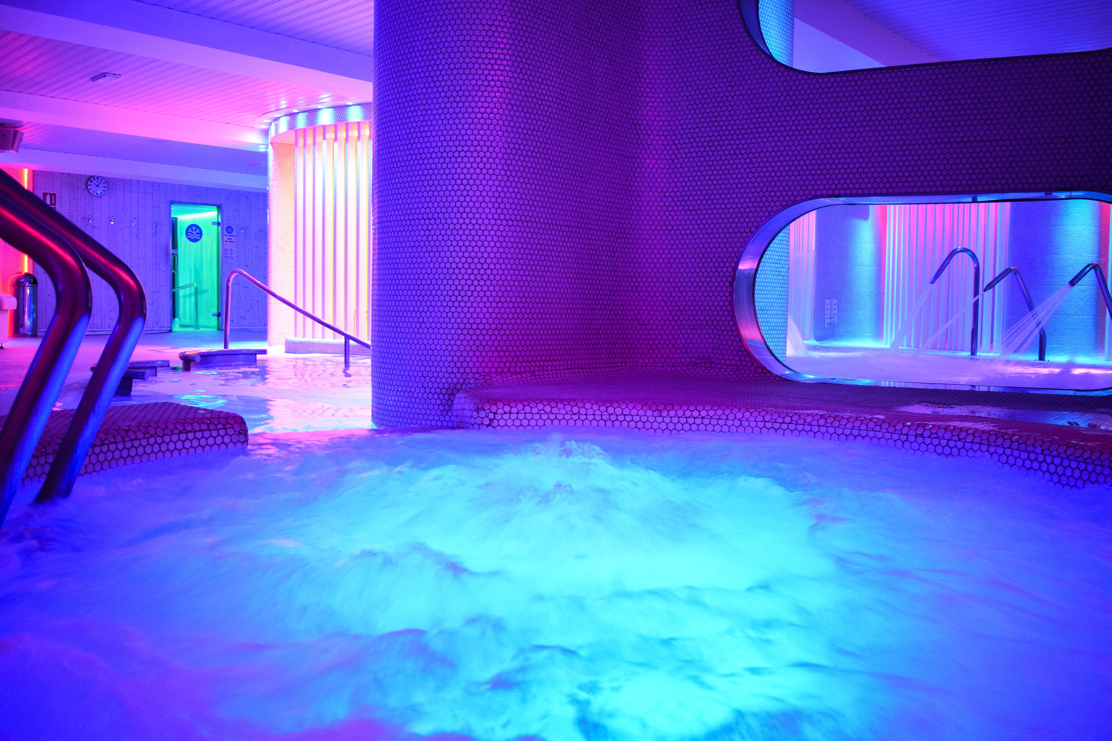 A modern spa area with a heated floor, a glass-enclosed sauna, and a staircase leading to an upper level.