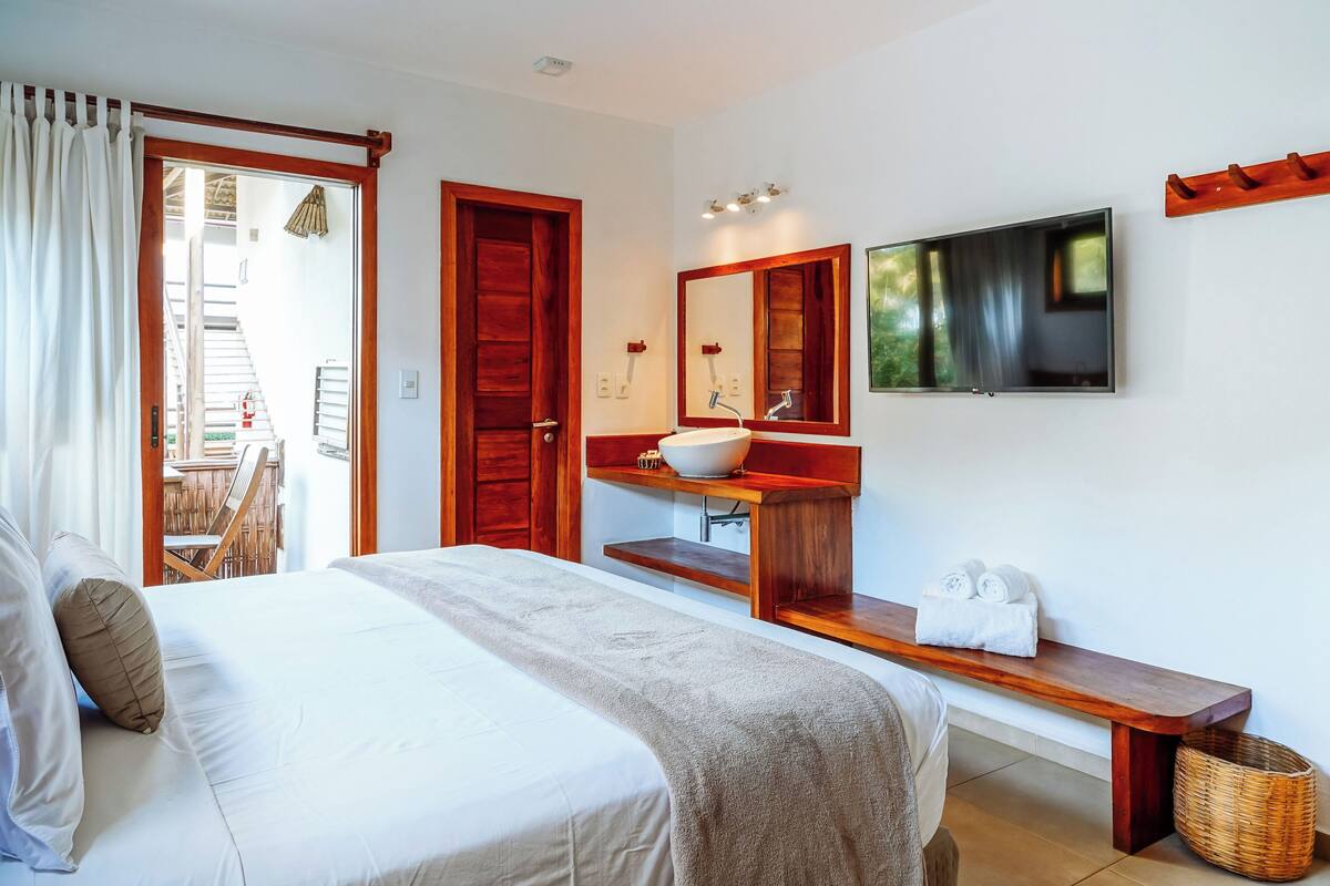 A bedroom with a bed, a wooden bench, a sink, a mirror, and a television.