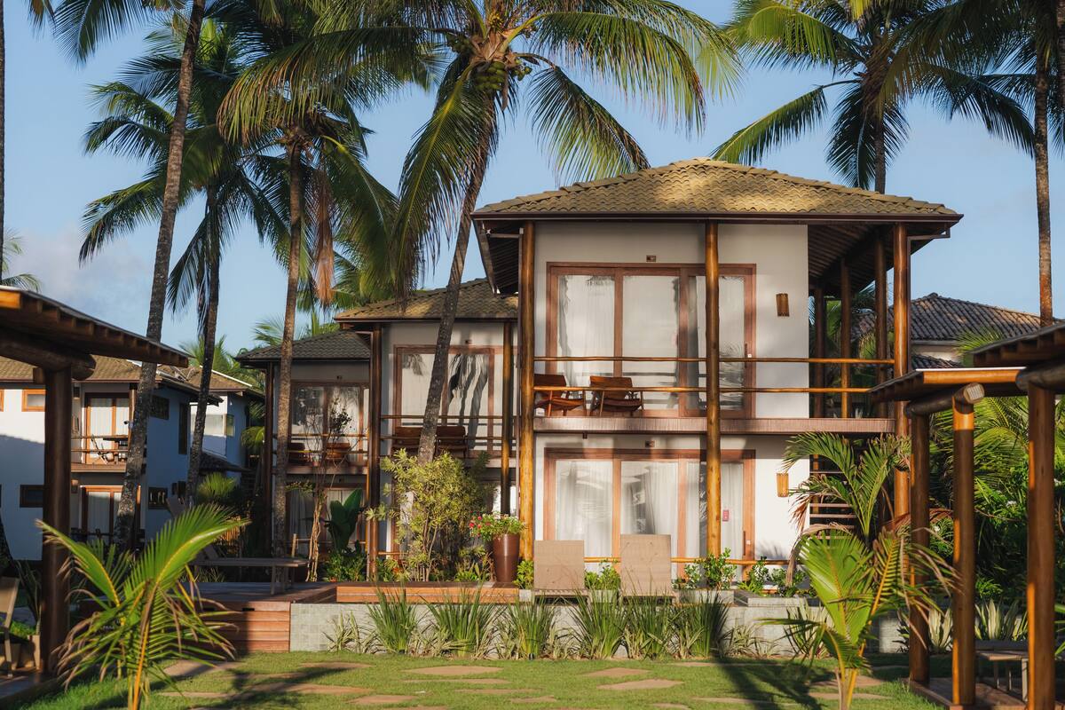 A two-story resort with a balcony, surrounded by palm trees and a well-maintained garden.