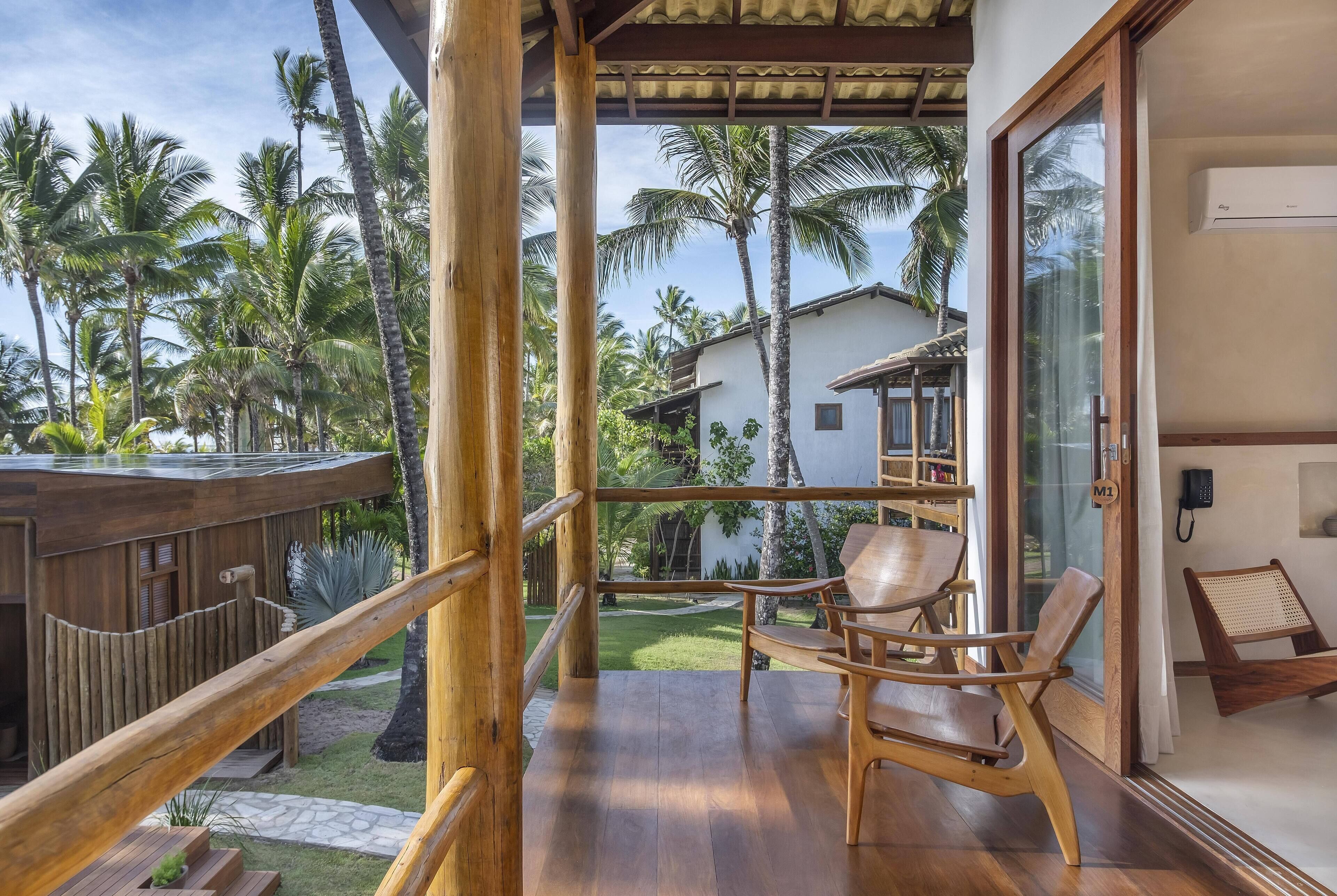 A wooden deck with chairs, a glass door, and a view of palm trees and a house.