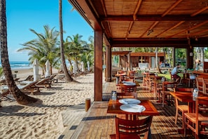 A beachside restaurant with wooden tables and chairs, palm trees, and a view of the ocean. - Dreamland Bungalows - Taipú de Fora - Barra Grande (Maraú)