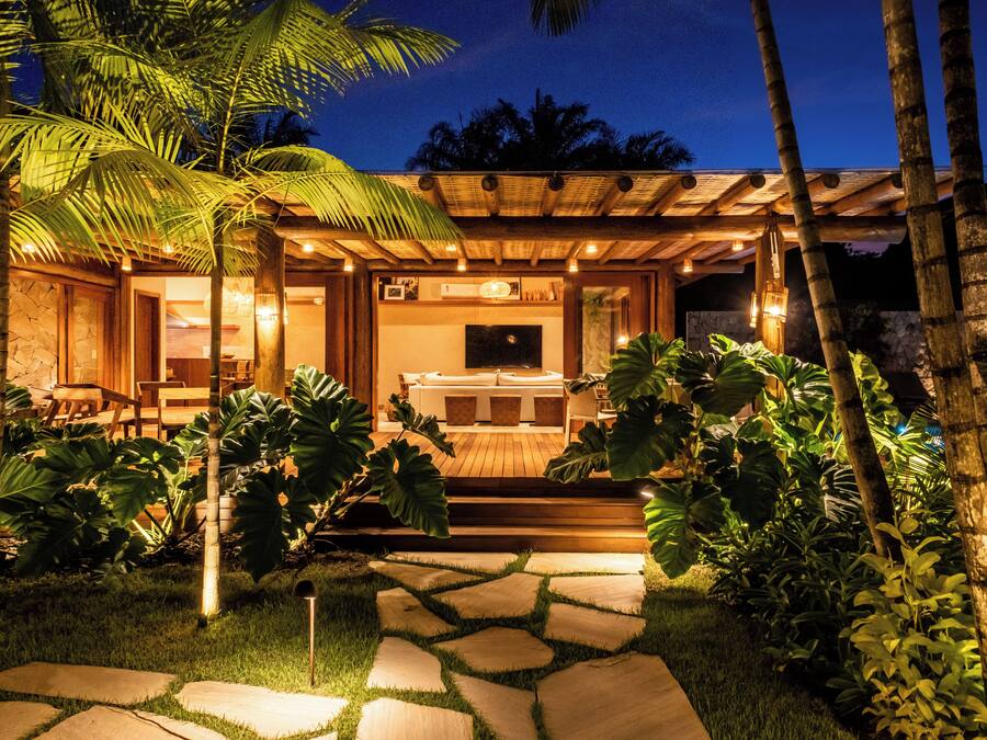 A well-lit outdoor seating area with a wooden pergola, stone pathway, and lush tropical plants.