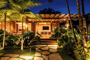 A well-lit outdoor seating area with a wooden pergola, stone pathway, and lush tropical plants. - Dreamland Bungalows - Taipú de Fora - Barra Grande (Maraú)