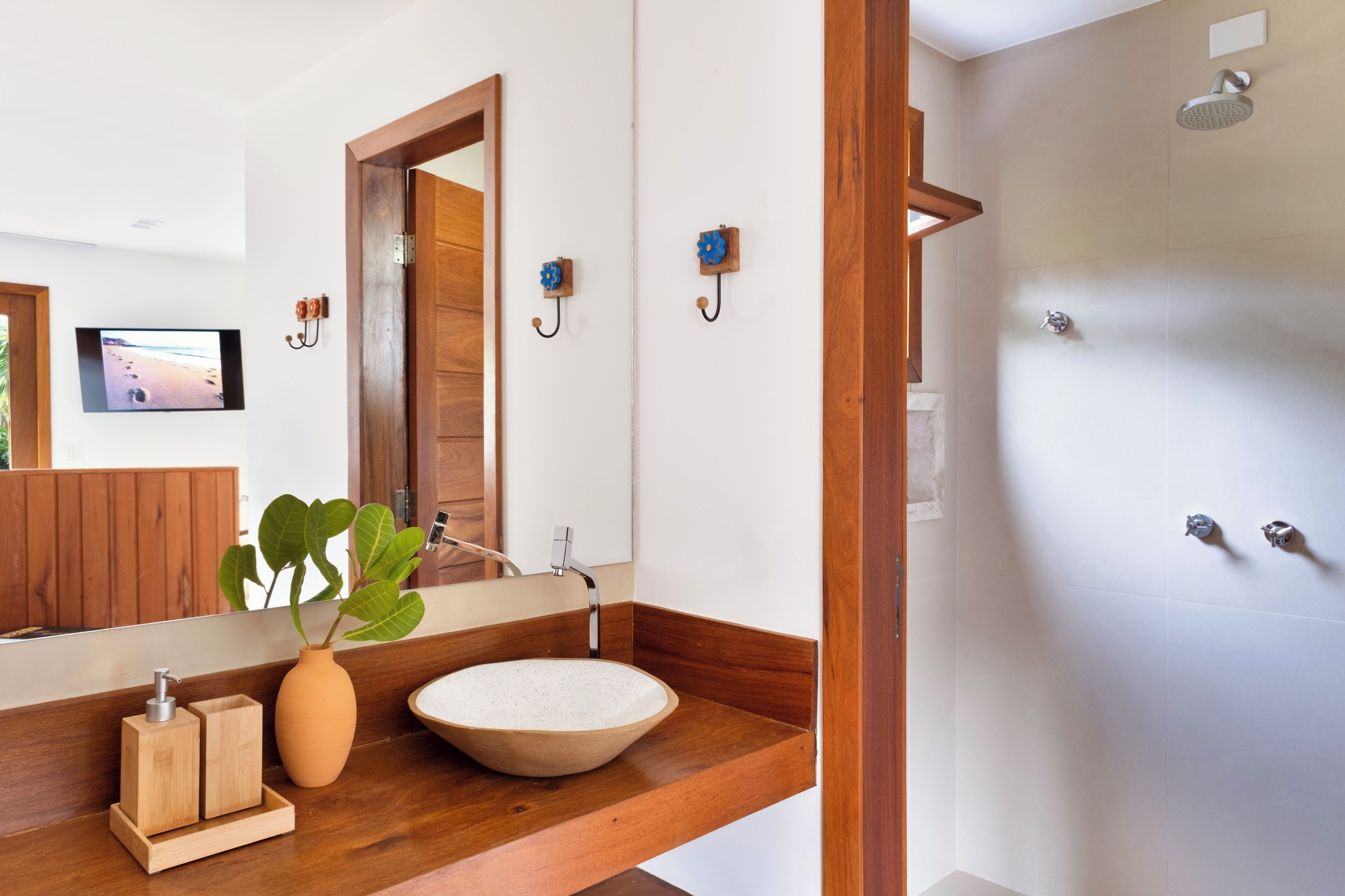 A bathroom with a wooden vanity, a round sink, a mirror, a shower, and a television on the wall.