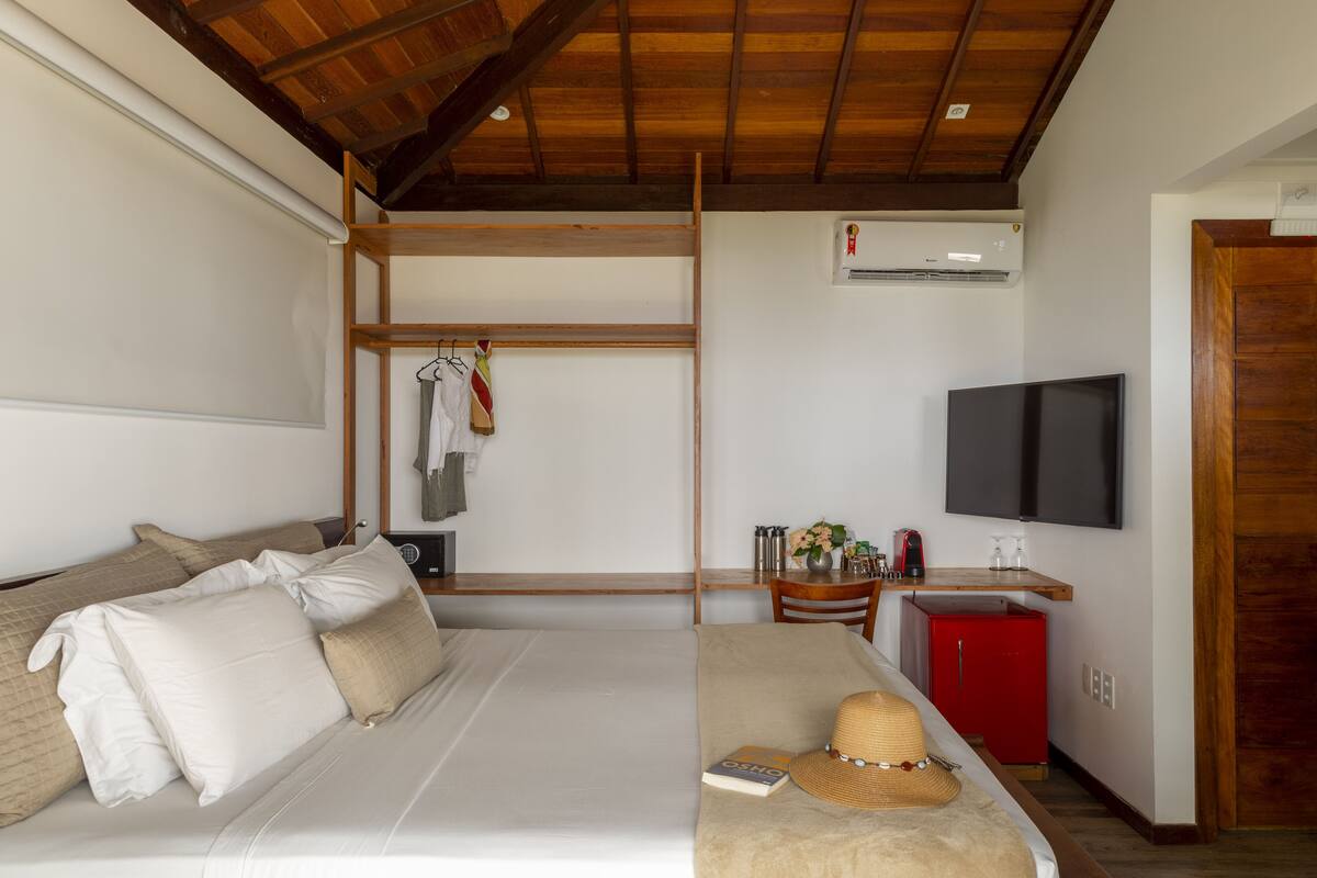 A hotel room with a bed, a TV, a red minibar, and a wooden ceiling.