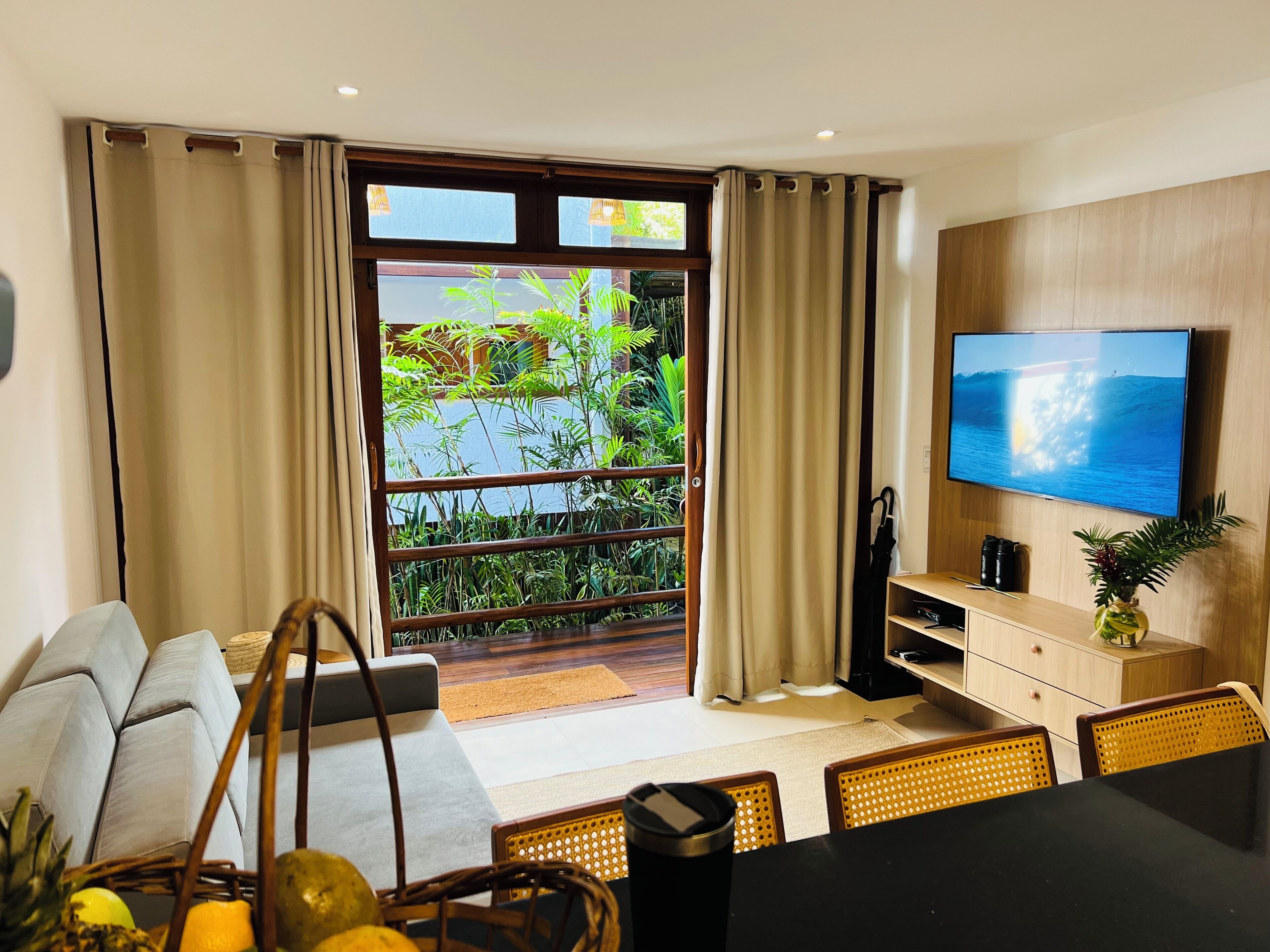 Una sala de estar moderna con sofá, mesa de comedor, sillas, televisor y un balcón con plantas.