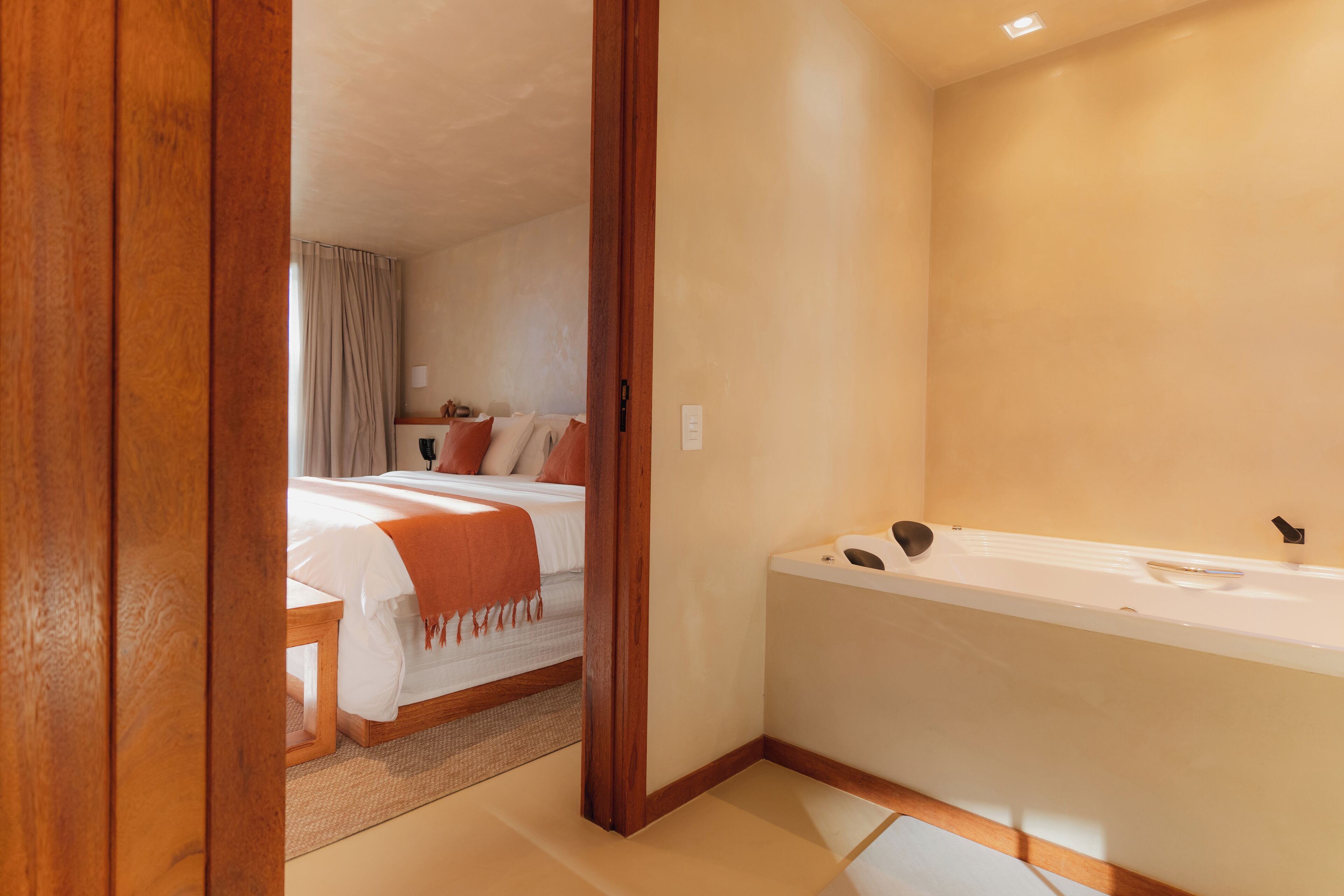 Una habitación de hotel con una cama grande, una zona de estar separada, una bañera y una puerta de madera.