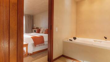 Una habitación de hotel con una cama grande, una zona de estar separada, una bañera y una puerta de madera.