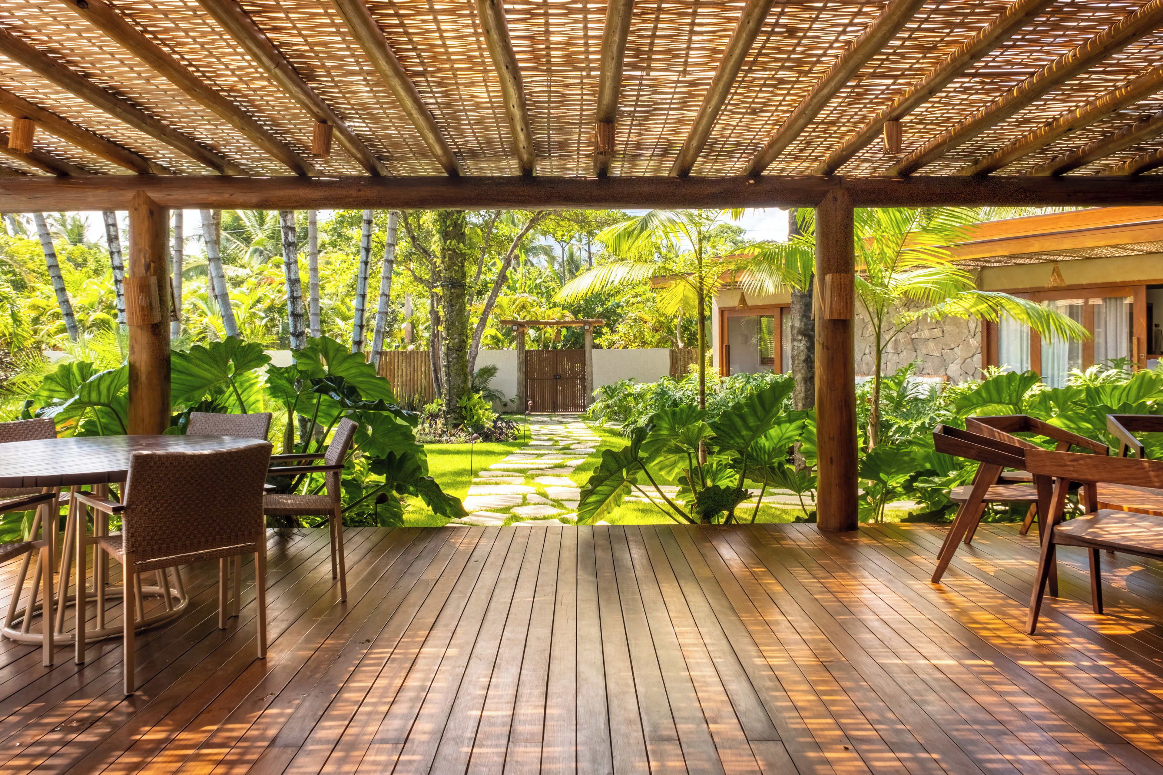 Una terraza de madera con una pérgola, rodeada de exuberante vegetación tropical y un sendero de piedra.