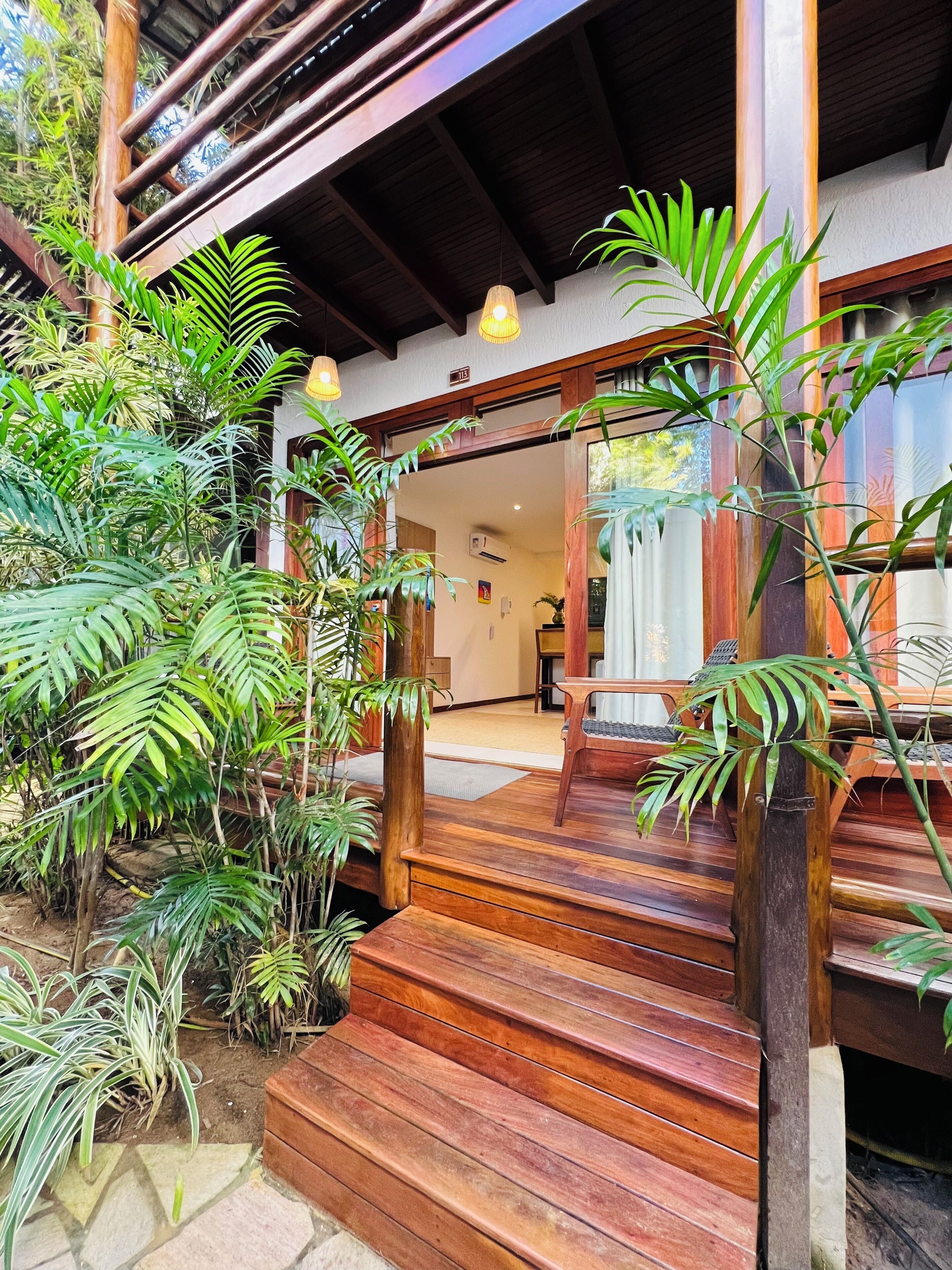 Una escalera de madera que lleva a un cuarto con vistas al exterior, rodeado de exuberante vegetación.