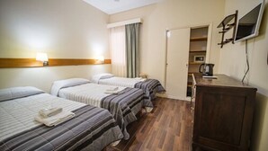 Une chambre d’hôtel avec trois lits, une tête de lit en bois, un téléviseur à écran plat fixé au mur et une armoire en bois.