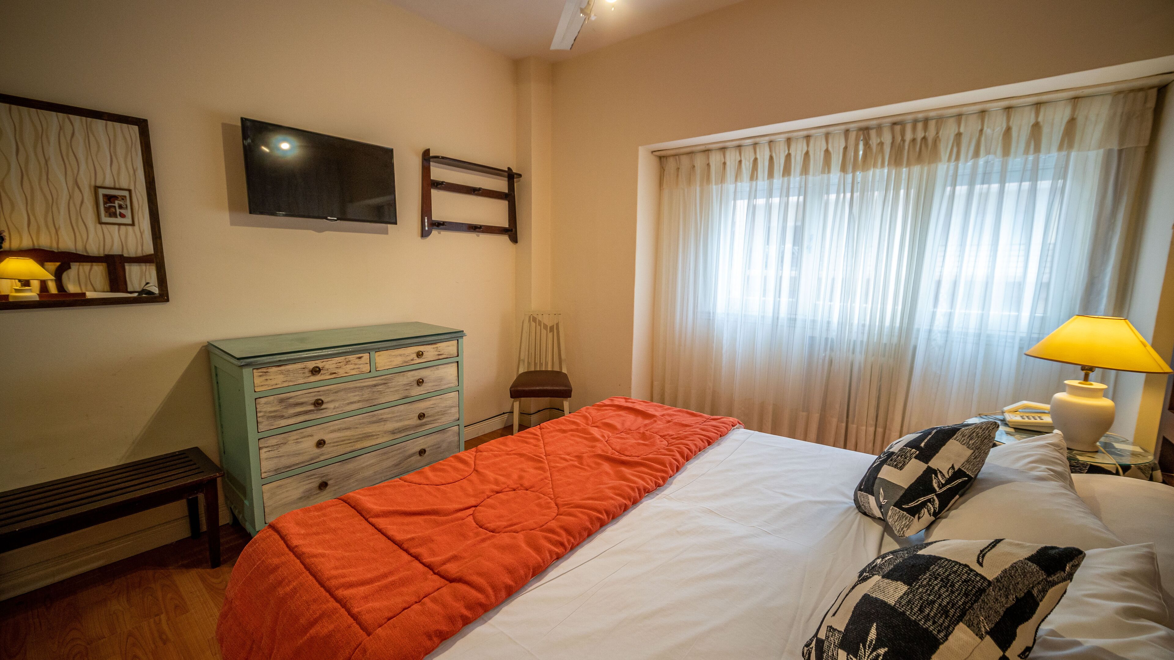 A hotel room with a bed, a dresser, a chair, a television, and a window with curtains.