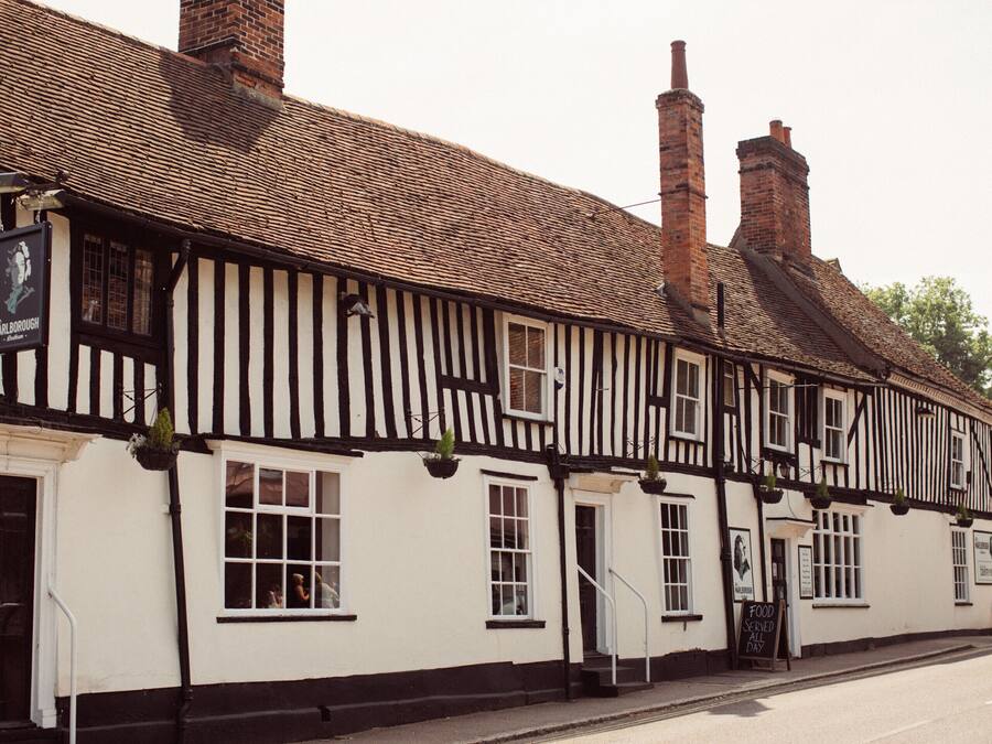 A traditional pub with a black and white exterior, multiple chimneys, and a sign indicating food is served all day.