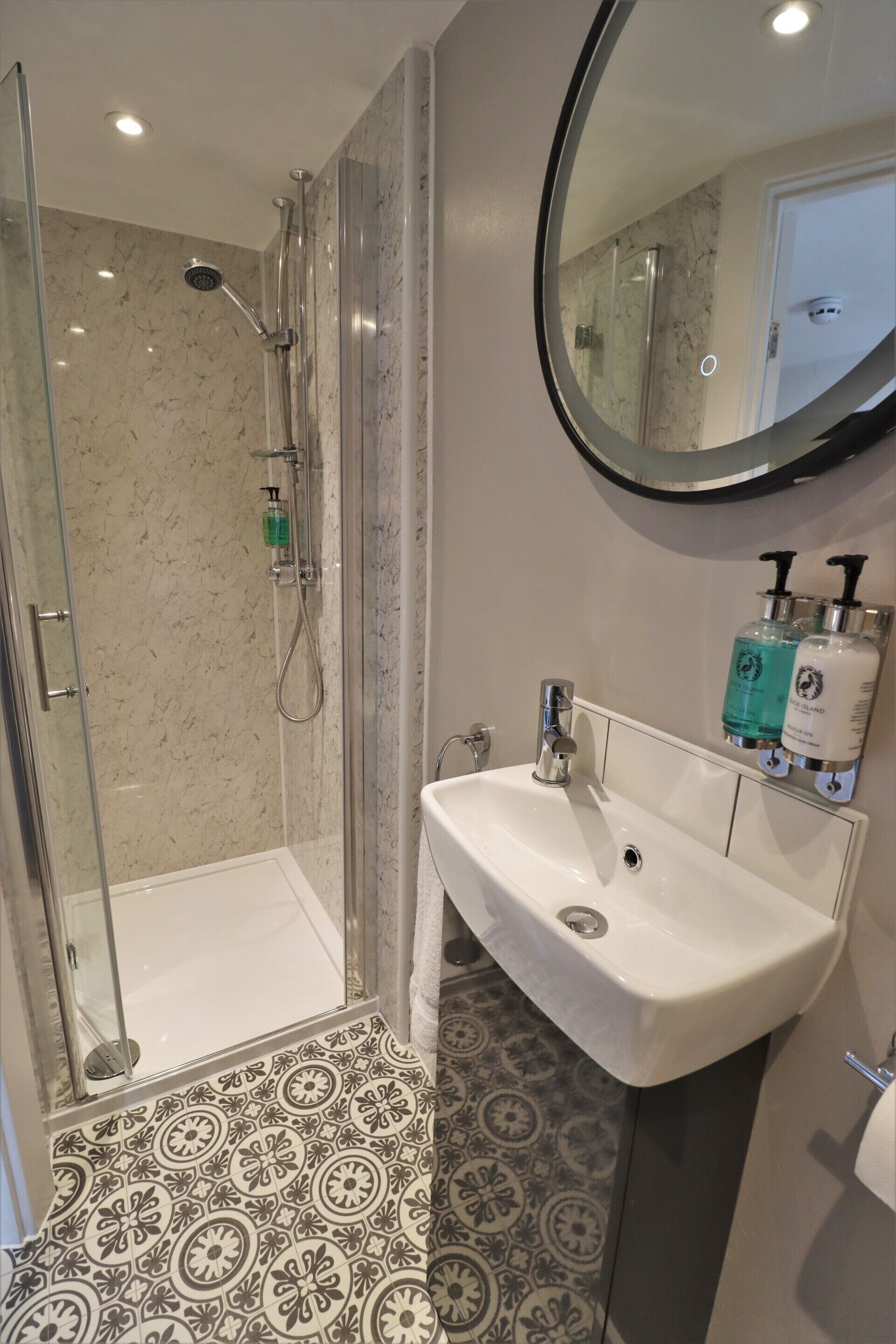 A bathroom with a glass-enclosed shower, a white sink, and patterned floor tiles.