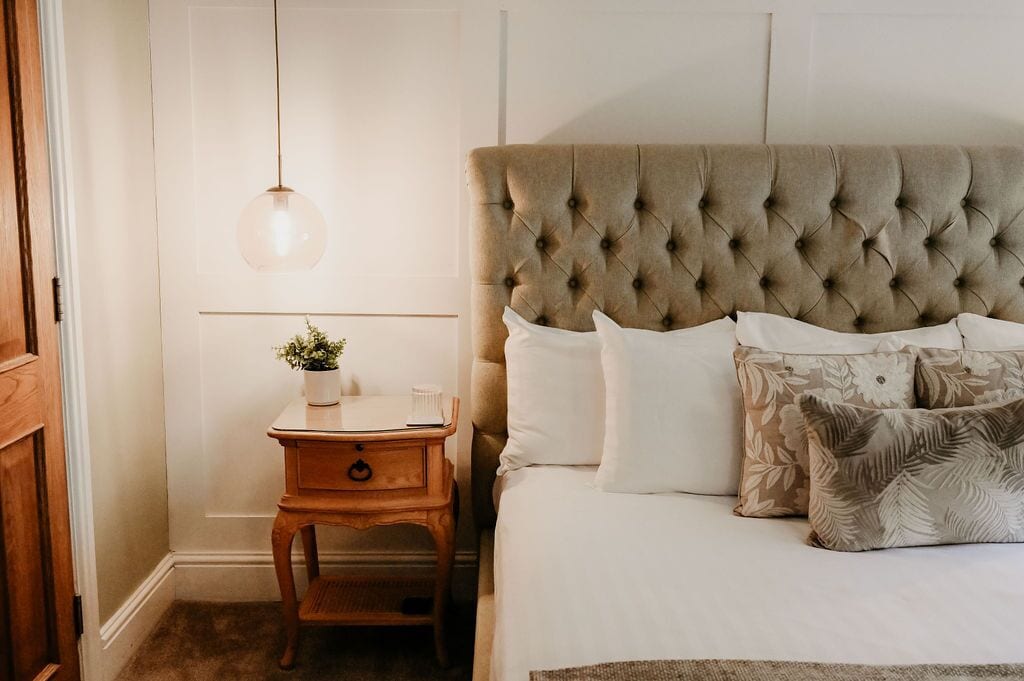 A bedroom with a tufted headboard, a bedside table with a plant, and a hanging light fixture.