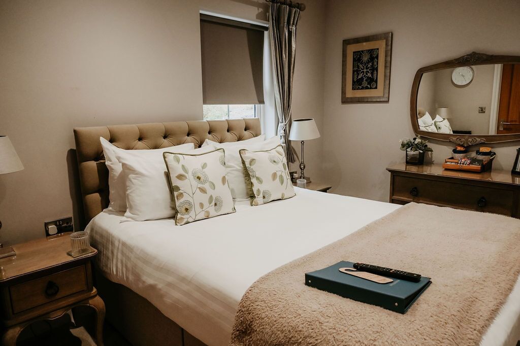 Habitación de hotel con una cama grande, una mesita de noche, una lámpara, un aparador, un espejo y una ventana con cortinas.