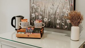 Een tafel met een glazen blad, een koffiezetapparaat, kopjes en een bakje koffiepads.