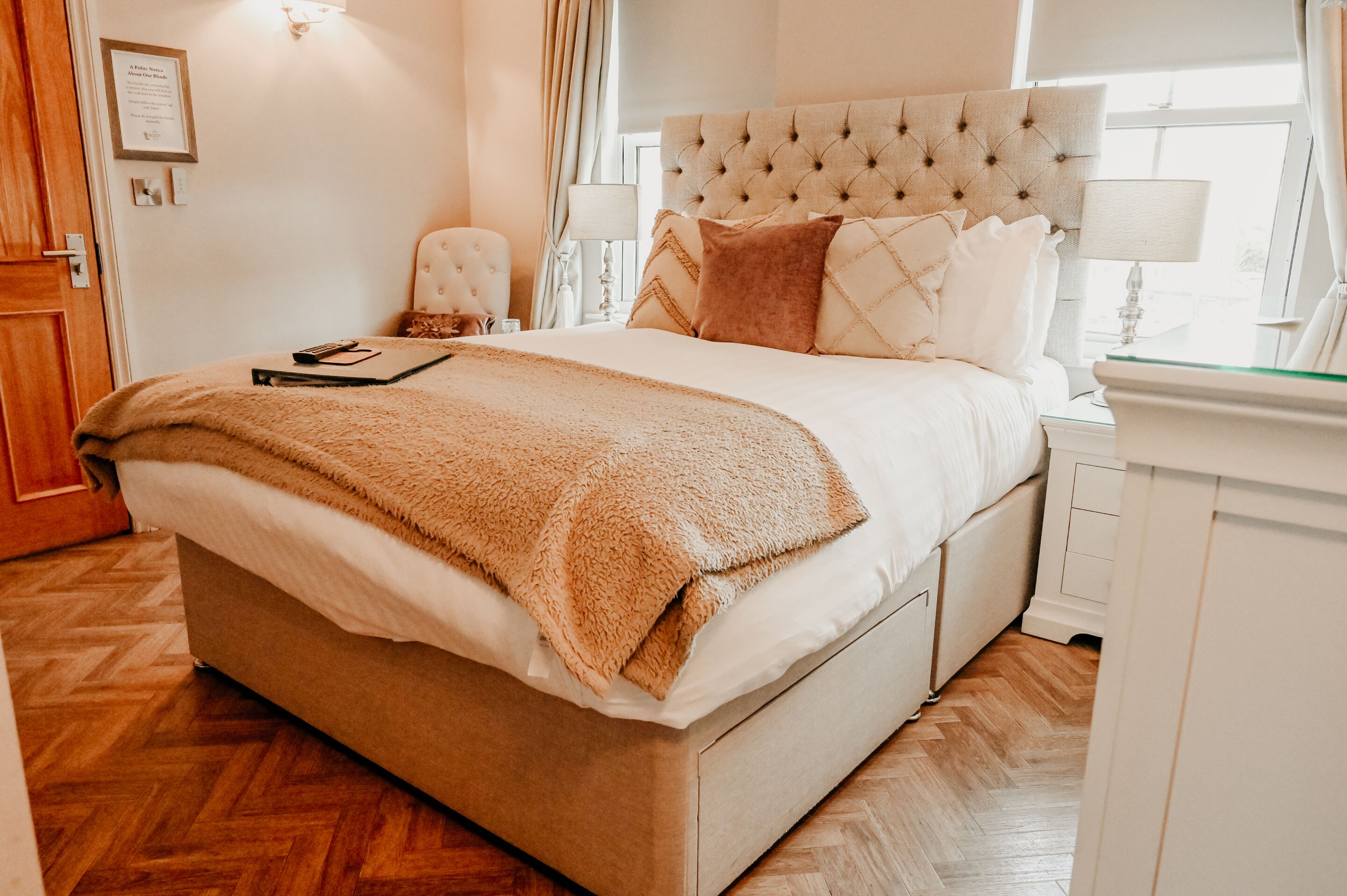 Een keurig opgemaakt slaapkamer met een groot bed, een nachtkastje, een stoel en een raam met gordijnen.