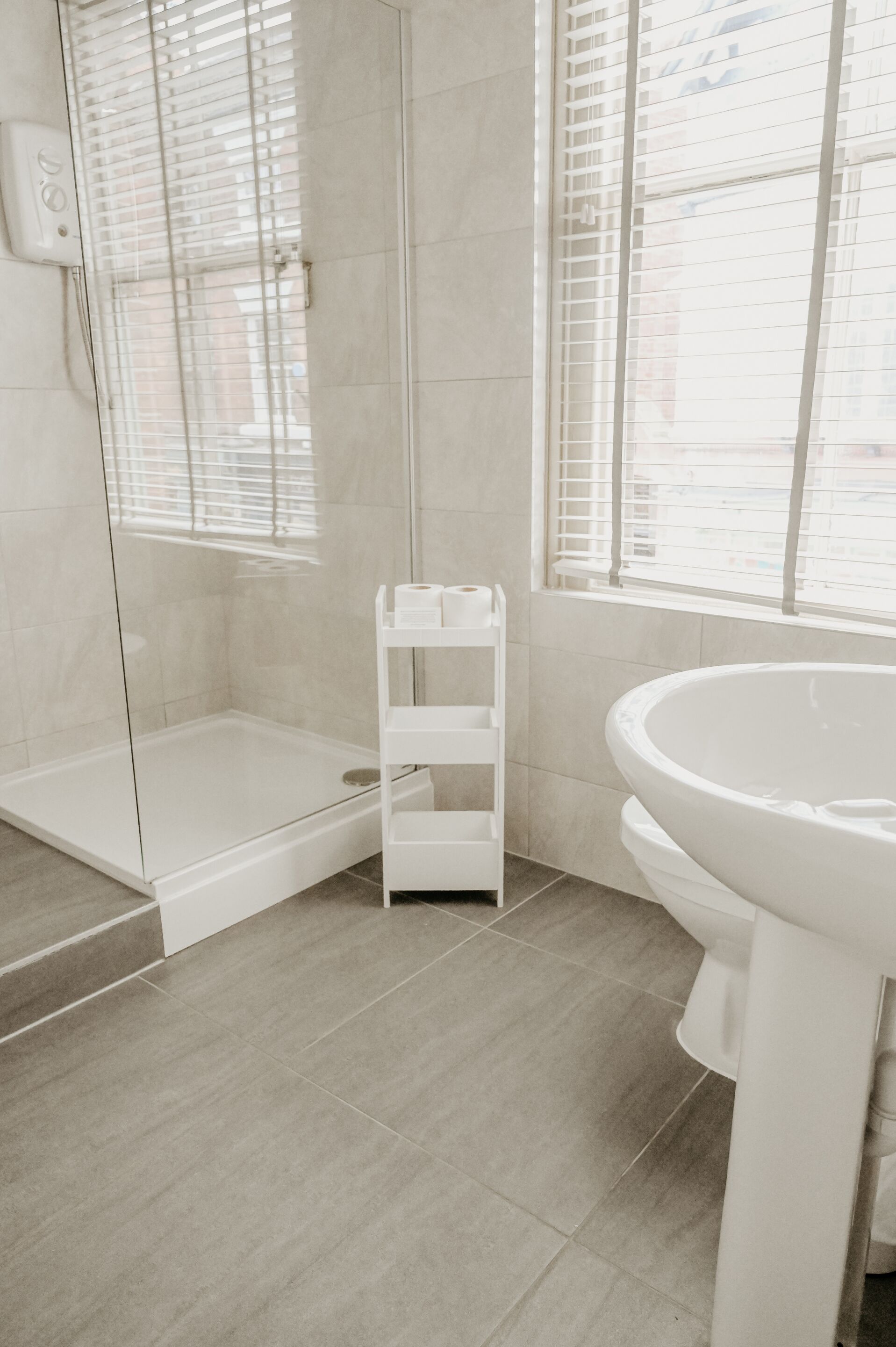 Un baño moderno con cabina de ducha de vidrio, un lavamanos blanco y una ventana con persianas.