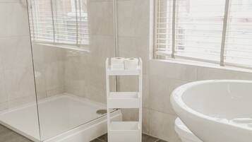 Un baño moderno con cabina de ducha de vidrio, un lavamanos blanco y una ventana con persianas.