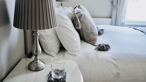 Een netjes opgemaakt slaapkamer met een bed, kussens, een bedlampje en een glas water op een nachtkastje.