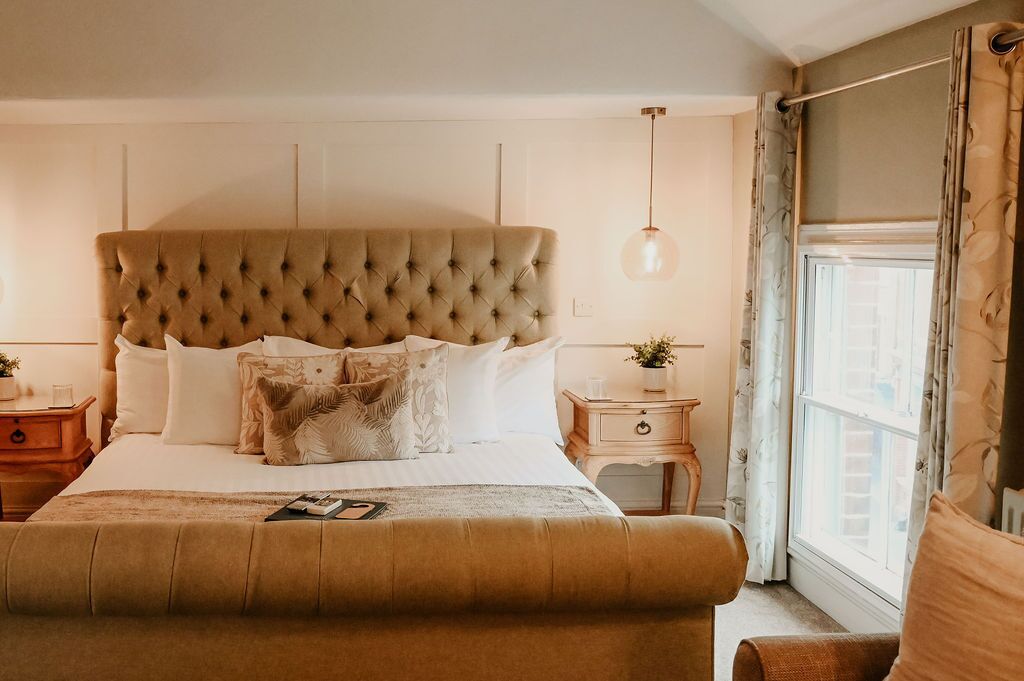 A bedroom with a tufted headboard, a bed with white linens, a bedside table with a lamp, and a window with curtains.