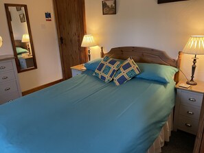 A neatly made bed with blue bedding and patterned pillows, flanked by bedside tables with lamps, a dresser, and a mirror. - Middle Flass Lodge (Clitheroe)