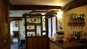 Un área de bar rústica con vigas de madera, una barra con botellas y un comedor al fondo.