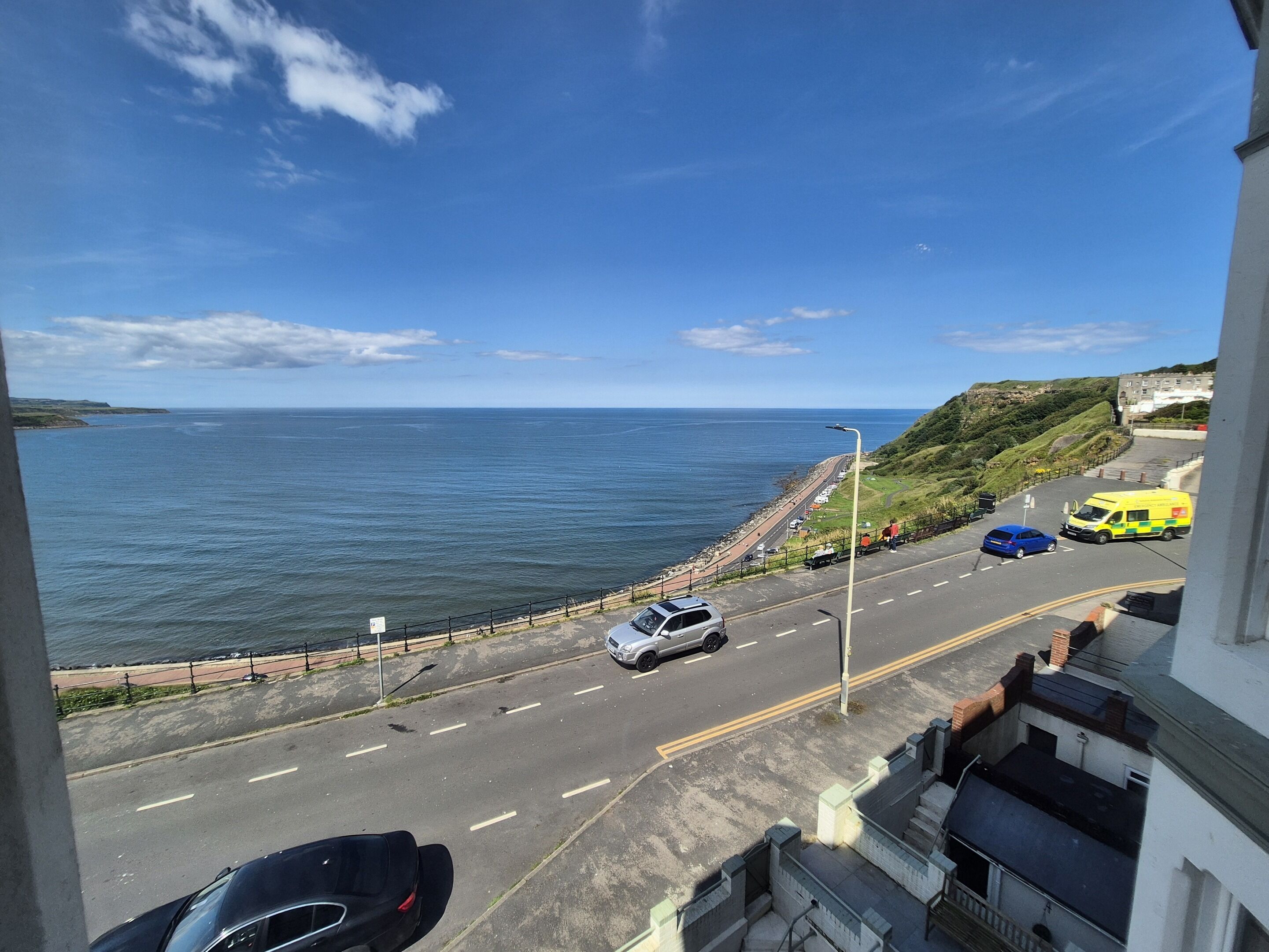 A coastal road with vehicles, a sea view, and a hilly landscape.