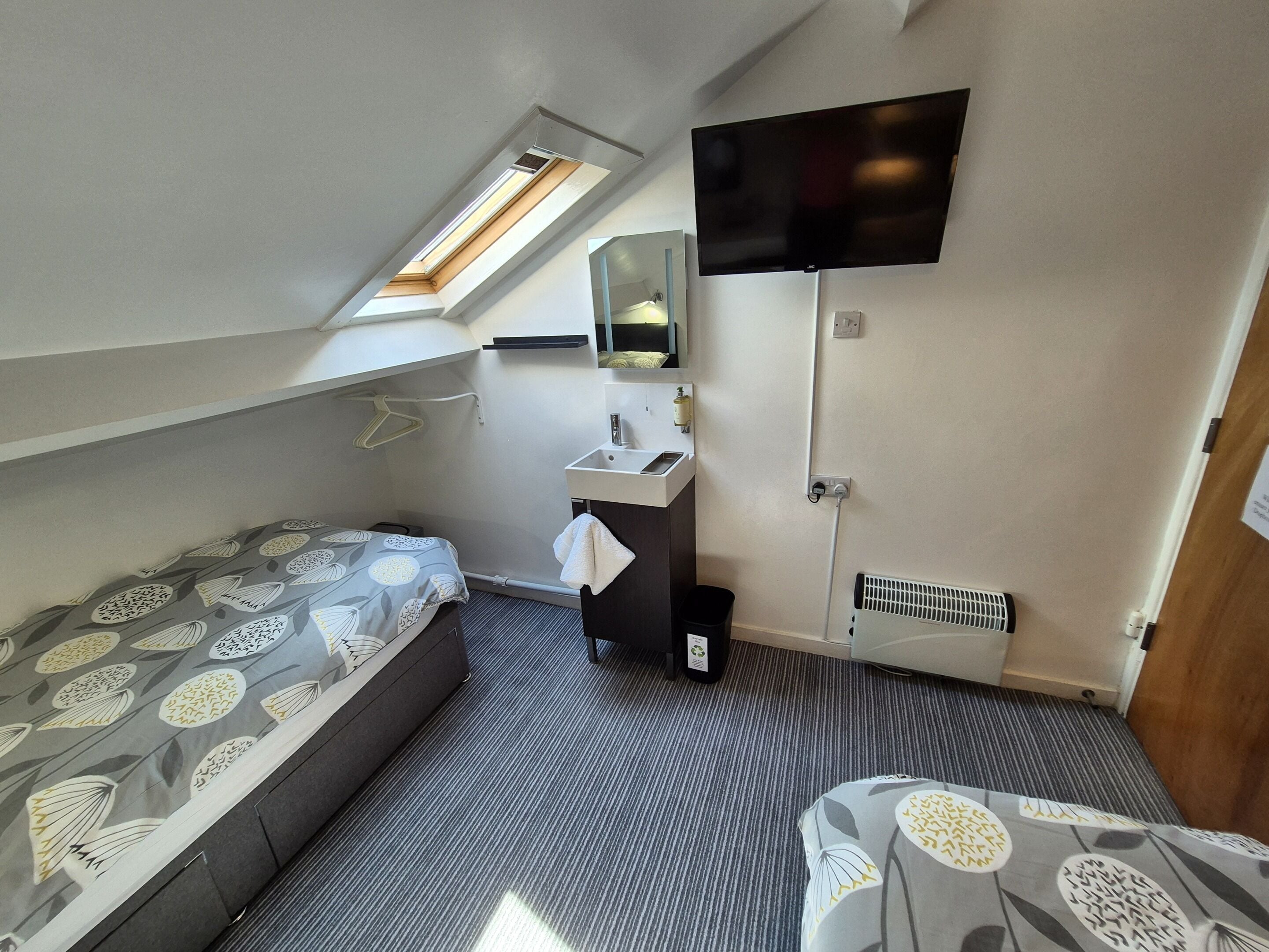 A compact room with a bunk bed, a small bathroom with a sink, a mirror, and a flat-screen TV mounted on the wall.