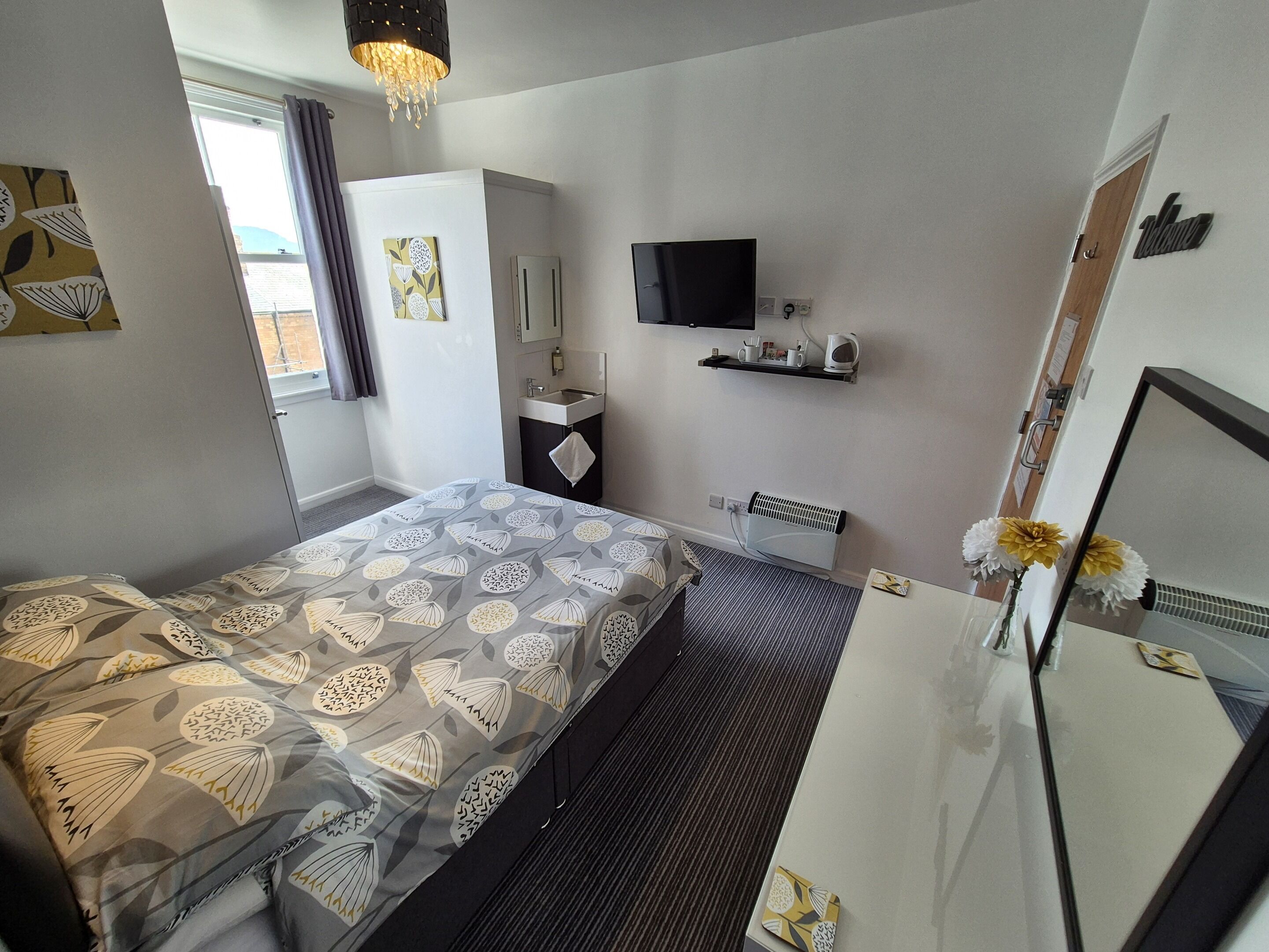 A hotel room with a bed, a desk, a TV, a mirror, and a window with curtains.