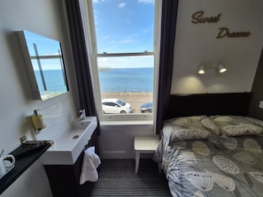 A hotel room with a bed, a bedside table, a window with a view of the sea, a bathroom with a sink, and a mirror. - Miricia Guest House (Scarborough)