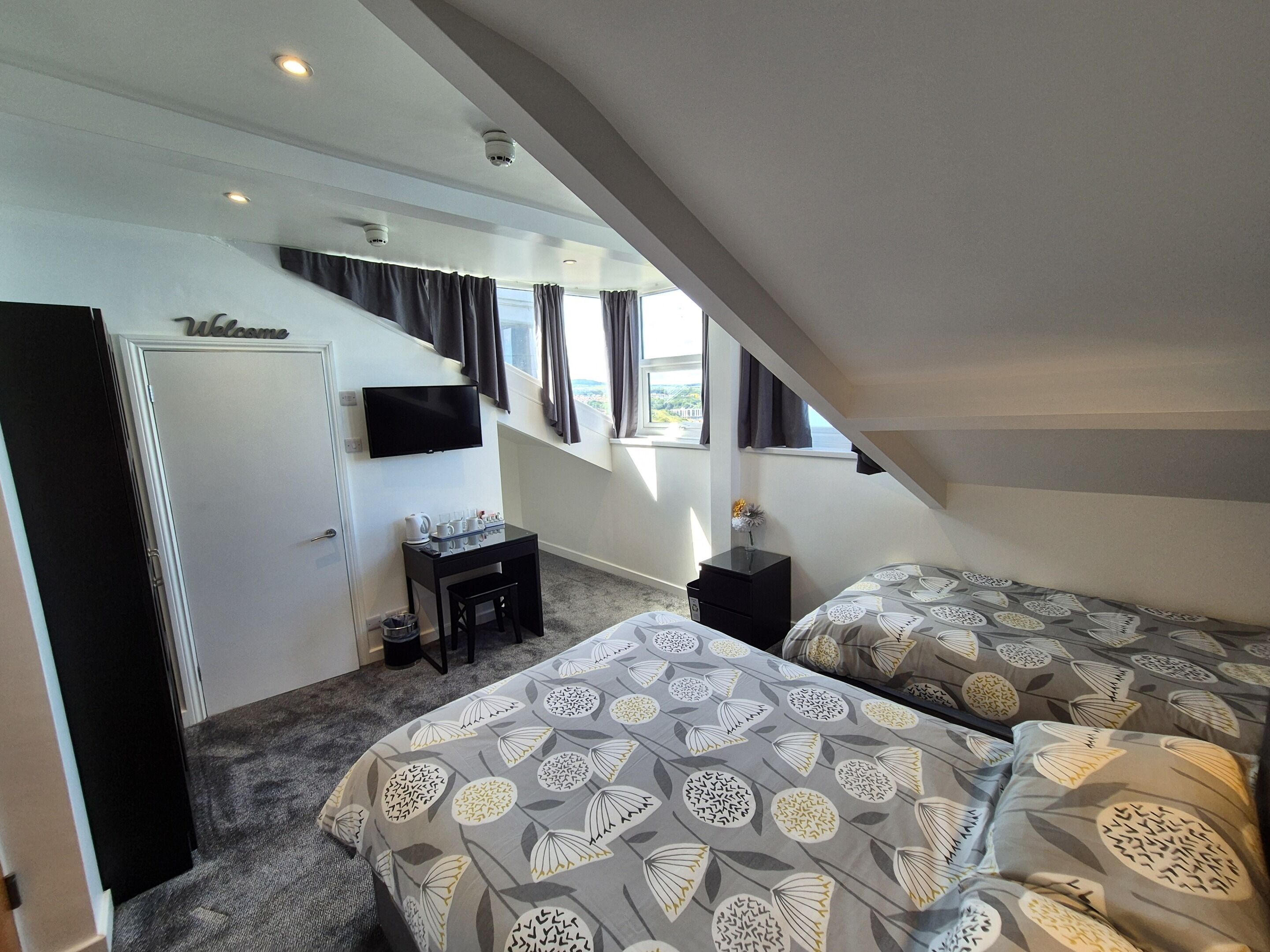 Een hotelkamer met een bureau, twee bedden, een televisie en uitzicht op de omgeving.