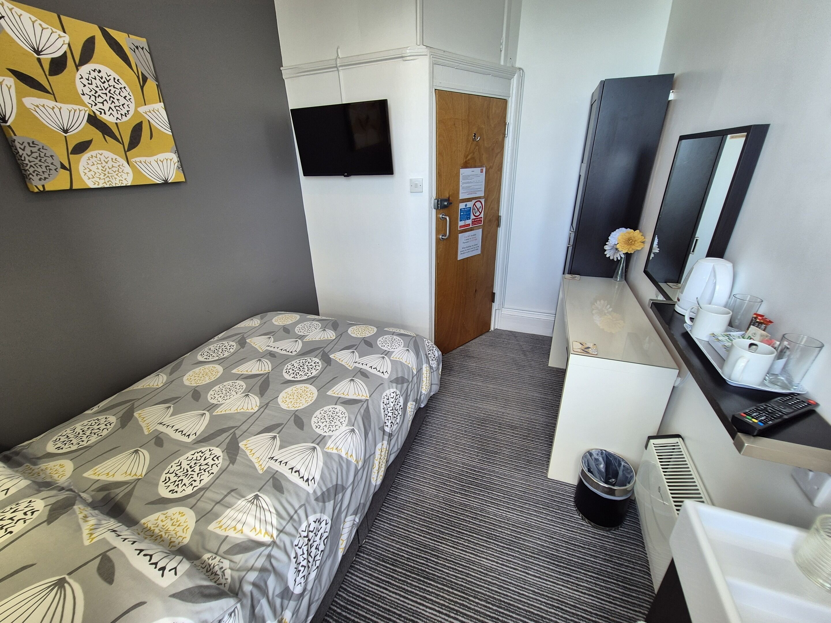 Een hotelkamer met een bed, een bureau, een spiegel, een prullenbak en een tv aan de muur.