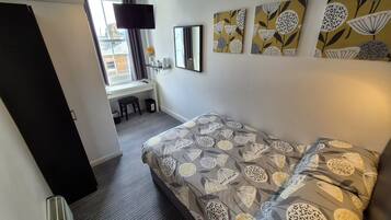 Quarto com cama, escrivaninha, cadeira e janela.