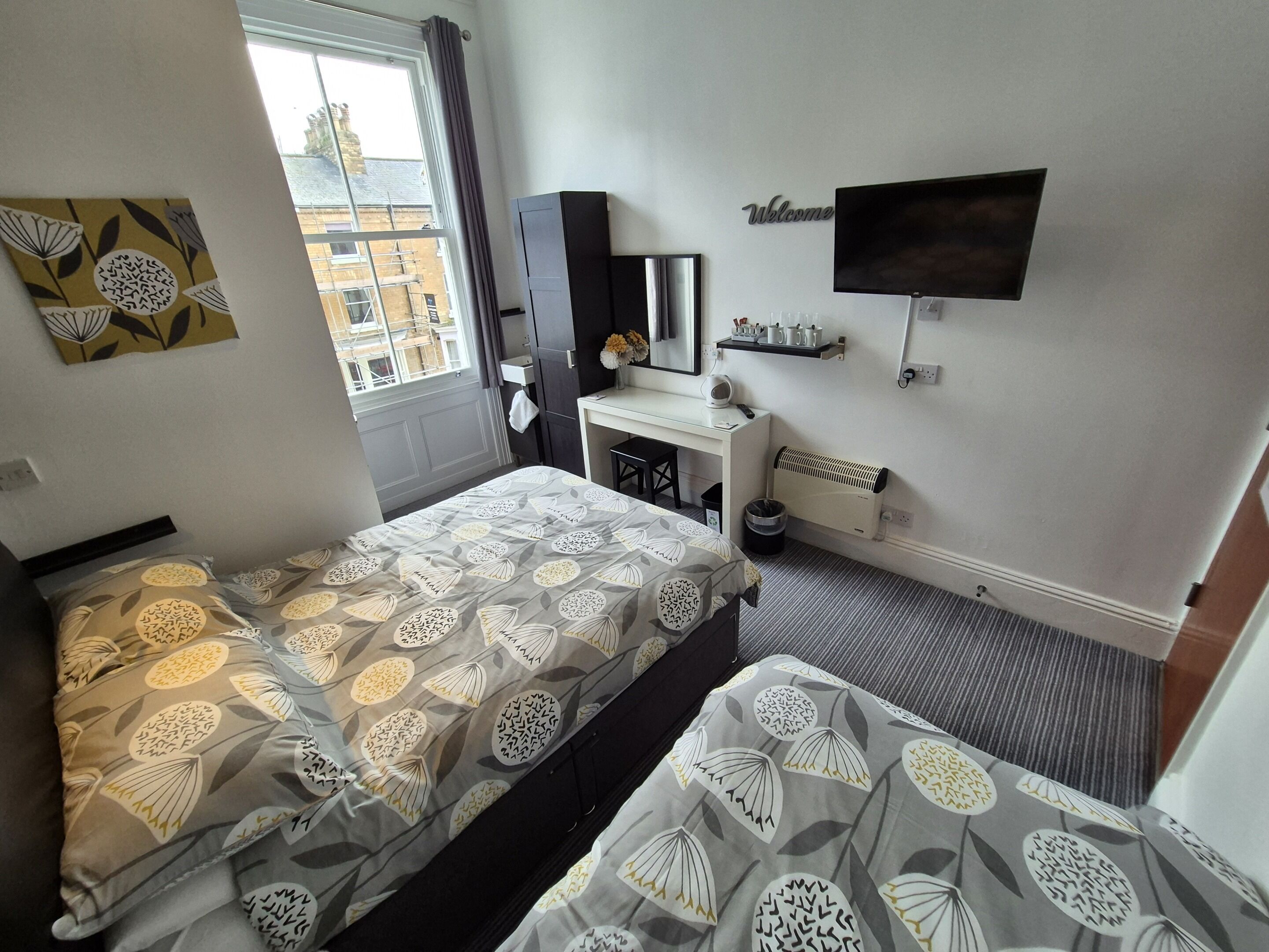 A hotel room with two beds, a desk, a chair, a TV, and a window with a view of buildings.