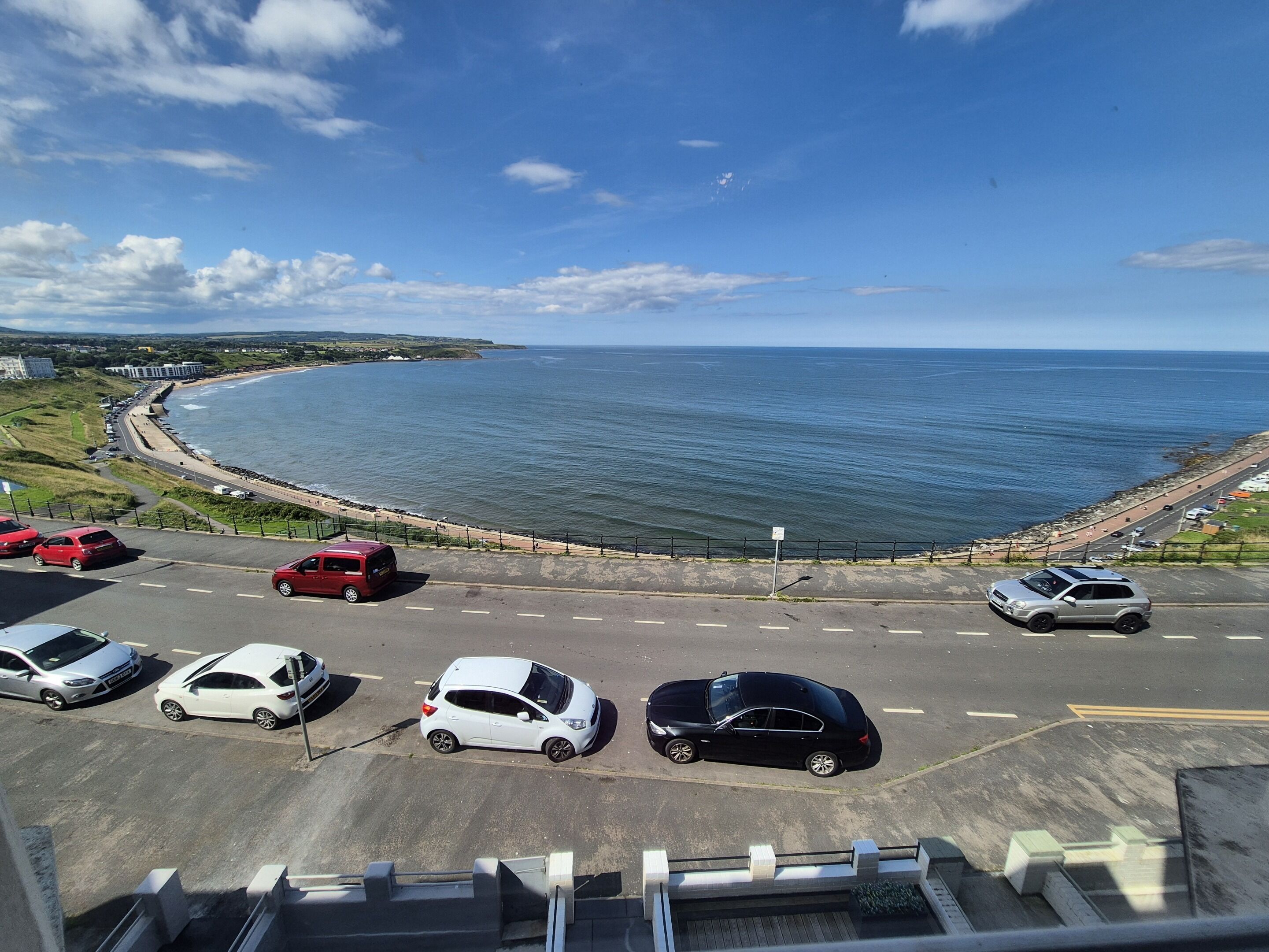 A coastal road with parked cars and a view of the sea.