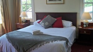 A neatly made bed with a grey throw blanket, red and grey pillows, and a white duvet. There are two bedside tables with lamps and a clock on one. A framed picture hangs above the bed. - Nelson and Railway Inn (Nottingham)