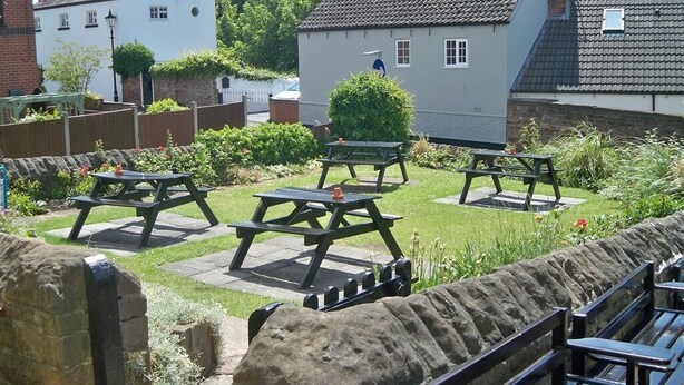 A courtyard with picnic tables, a stone wall, and a white building with a tiled roof. - Nelson and Railway Inn (Nottingham)
