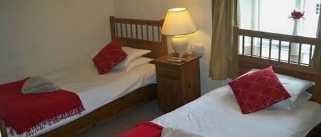 Two single beds with red bedding, a bedside lamp, a wooden nightstand, and a window with curtains.