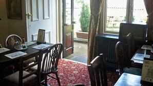 A dining area with a wooden table and chairs, a red patterned carpet, and a window with curtains. - Nelson and Railway Inn (Nottingham)