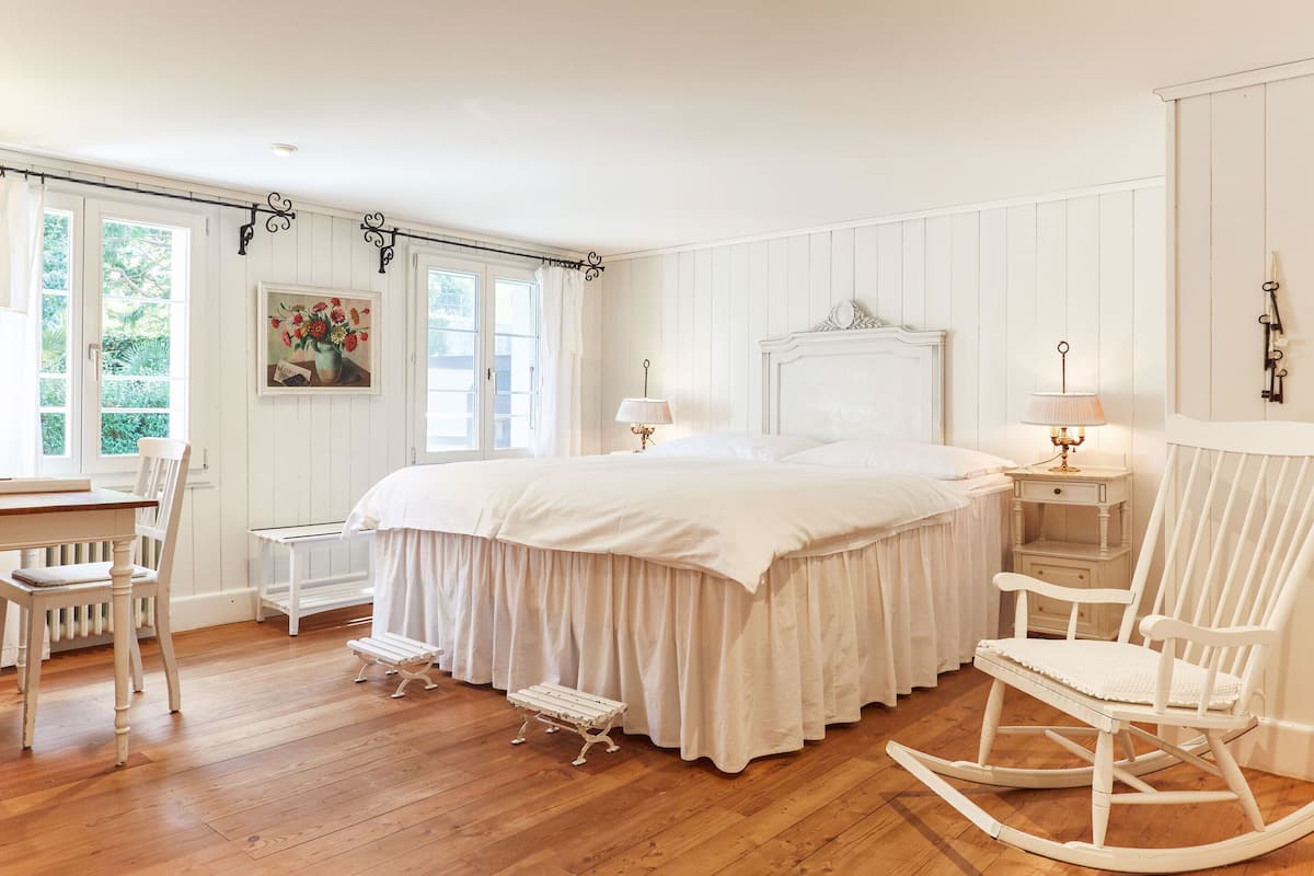 Ein Schlafzimmer mit einem großen Bett, weißen Möbeln und einem Schaukelstuhl.